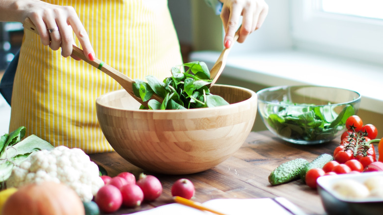 Woman preparing salad in wooden bowl