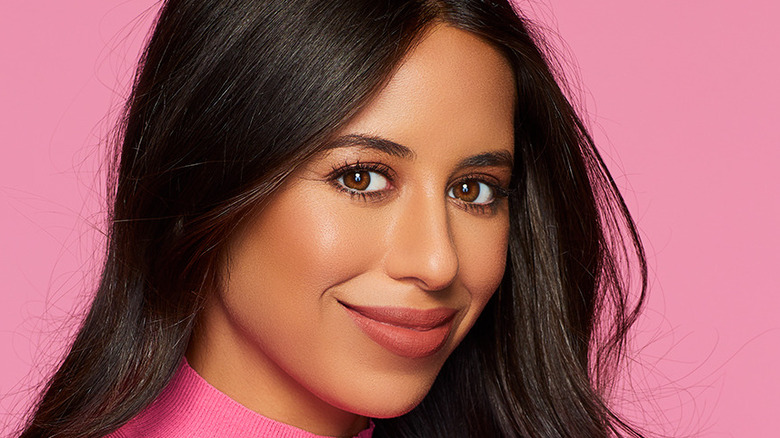 Naz Perez standing against a pink wall, smiling