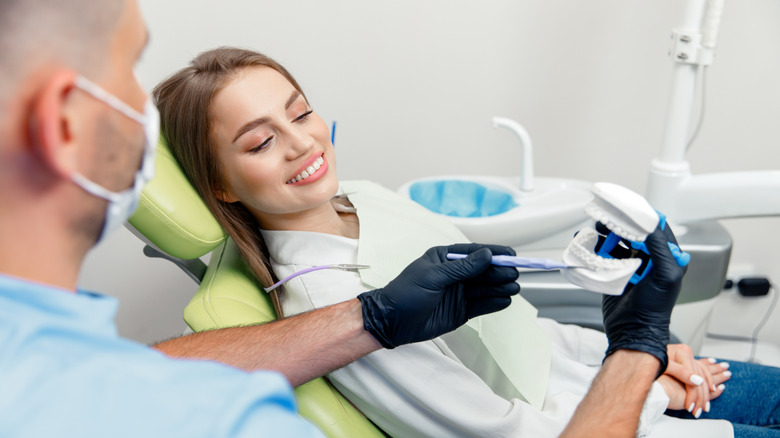 A Gen Z woman sitting in a dentist's chair while the dentist shows a tooth model