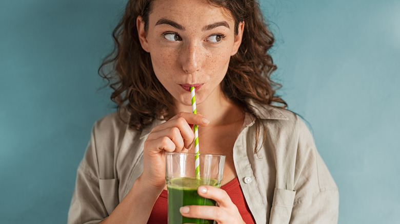 woman sips green juice with straw 