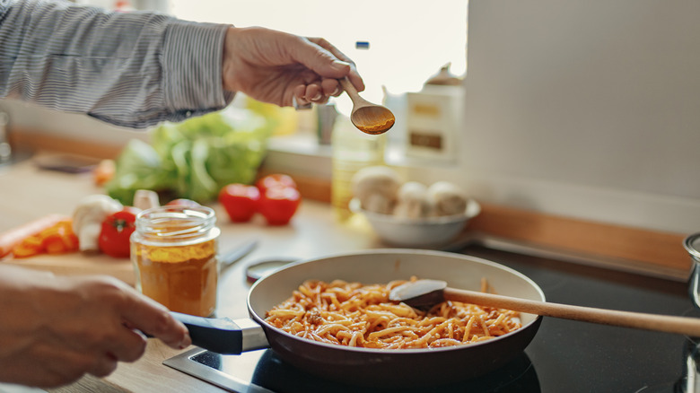 Hand sprinkling spoonful of spices over pasta