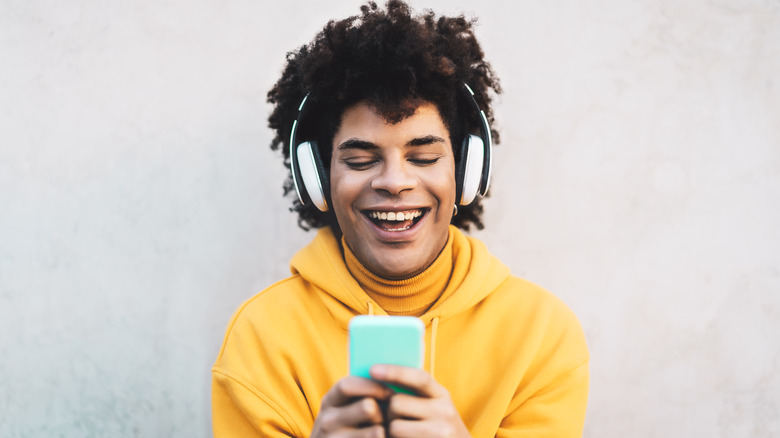 smiling person looking at smart phone with headphones on