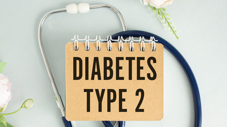 A doctor with a stethoscope around the neck writing the words "diabetes type 2" with a black sharpie