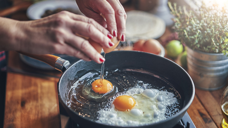 hands cracking egg in frying pan