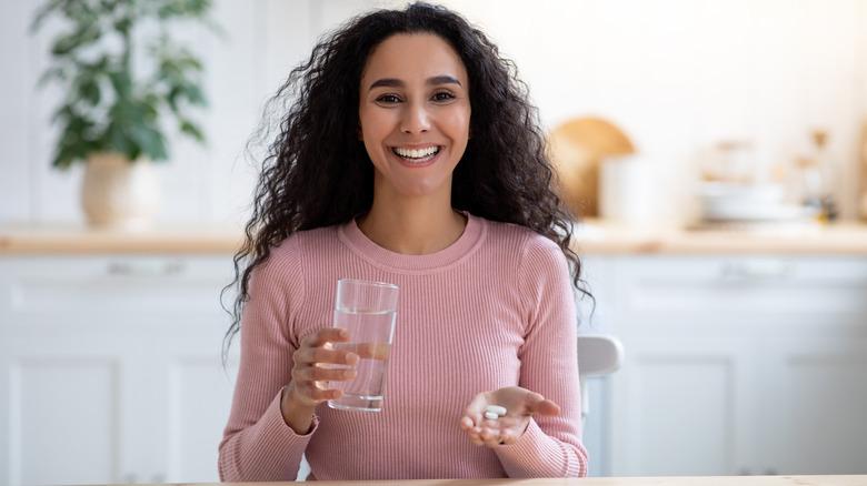 Smiling woman holding supplements and water