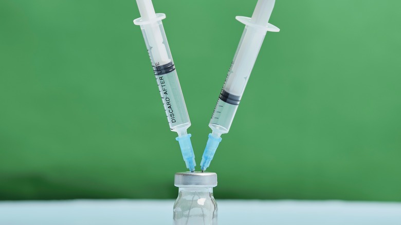 Two syringes in a vaccine vial on green background