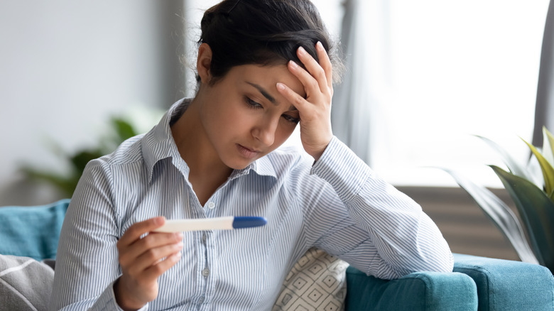 Unhappy woman looks at pregnancy test with her hand to her head