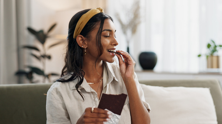 A woman eating a dark chocolate candy bar while sitting on her couch