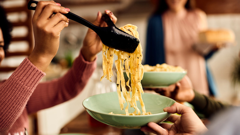 woman using tongs to add pasta to a plate