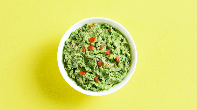 A bowl of guacamole on a yellow background