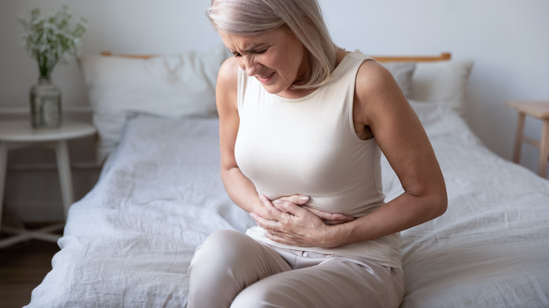 Woman sitting on bed clutching her stomach in pain