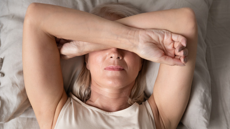 Woman laying down in bed covering her head with her arms in pain