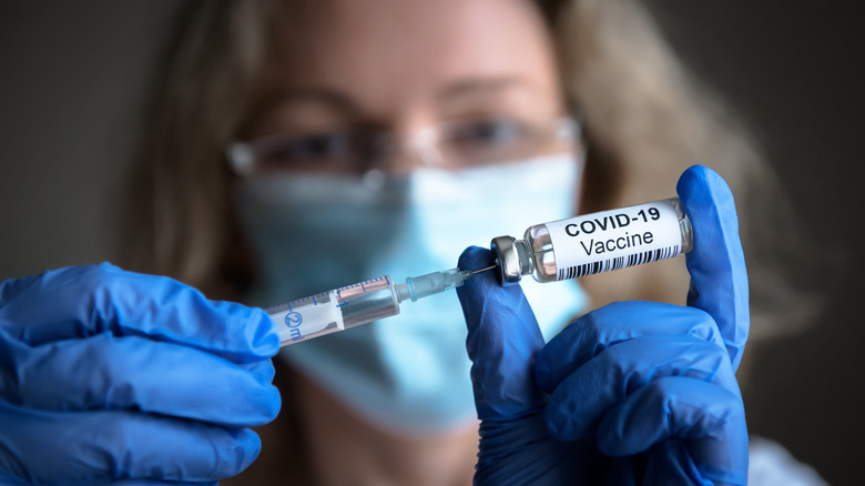 Medical provider filling a syringe from a bottle marked COVID-19 vaccine