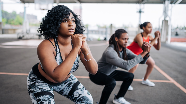 a man and two women doing air squats outside