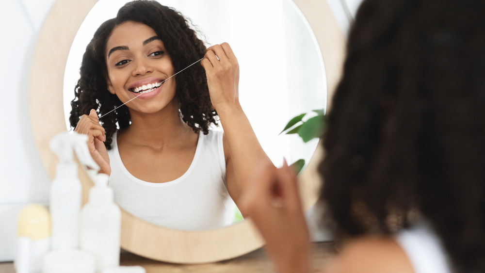 Woman smiling and flossing in mirror