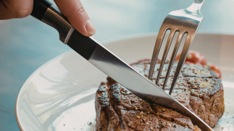 hands using fork and knife to cut steak