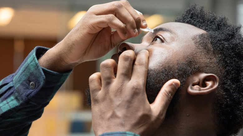 Man in flannel shirt opening up his left eye and using eye drops