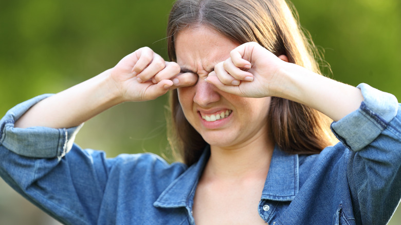 Woman wincing and holding her hands up to her eyes in pain