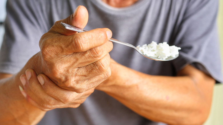 A man with shaky hands tries to feed himself