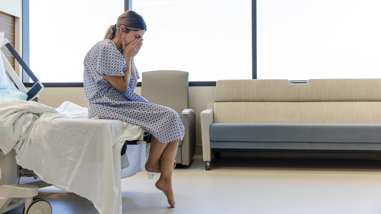 woman sitting at edge of hospital bed with head in hands