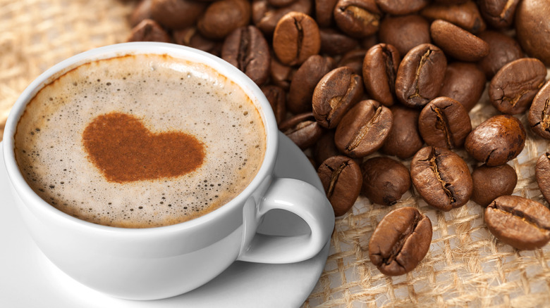 A white mug of black coffee with foam and coffee beans