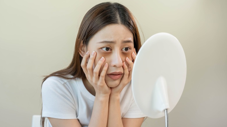 woman looking at her dry eyes in the mirror