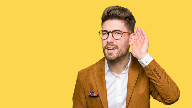 man wearing glasses smiling with hand over ear