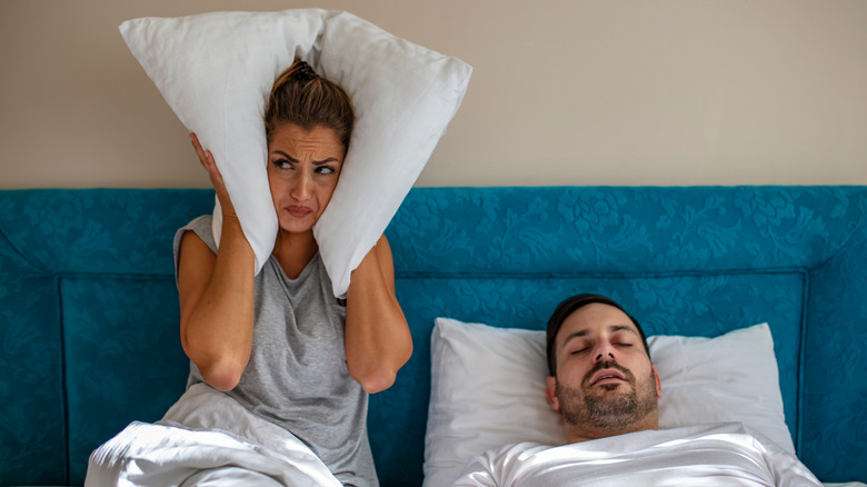 Woman holding pillow to ears as partner snores