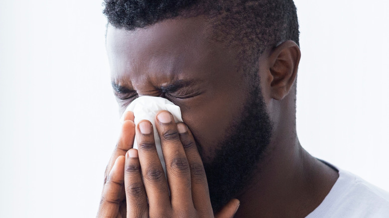 Man blows his nose against a white background