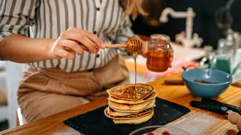 woman adding honey to pancakes