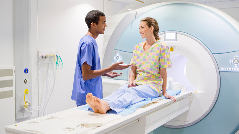 Healthcare professional speaking to smiling woman sitting up on CT scan table