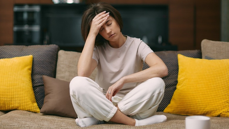 woman on couch holding head with eyes closed