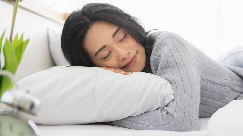 Woman asleep in bed holding her pillow and smiling next to a vase of purple flowers
