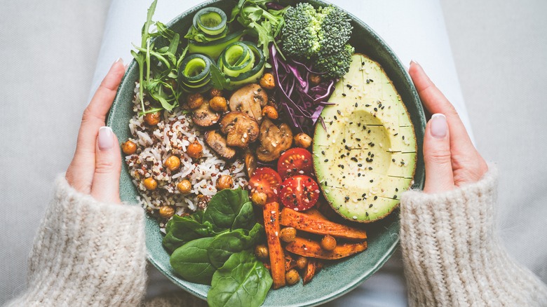 Someone holds a bowl filled with various fruits, vegetables, and plant based foods