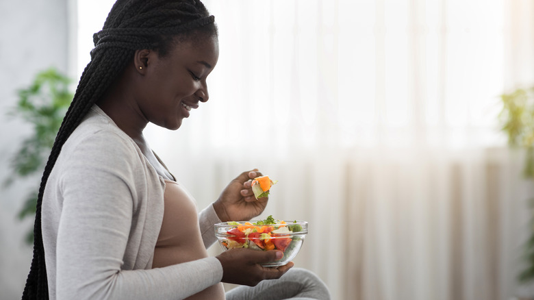 Pregnant woman eating on bed