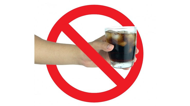Red circle and cross superimposed on hand holding soda glass