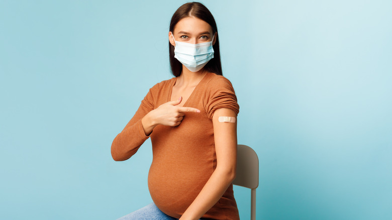Pregnant woman wearing mask, pointing to arm bandage