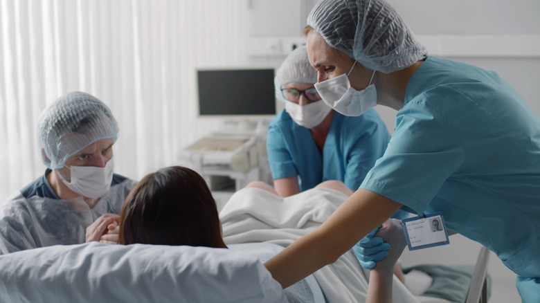 Woman giving birth in hospital surrounded by doctors wearing face masks