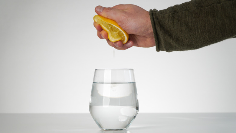 Hand squeezing half a lemon over a glass of water
