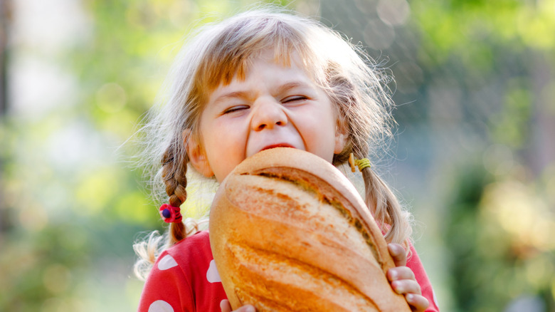 A happy little girl biting into a huge loaf of bread