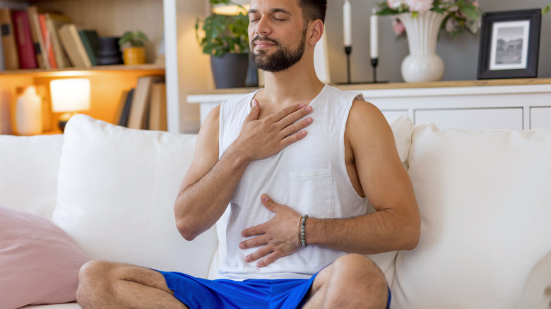 A peaceful man sitting on a sofa holding his stomach