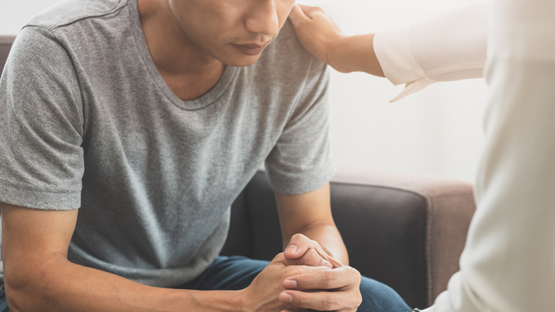 Young man sits on couch in front of a doctor who puts their hand on his shoulder