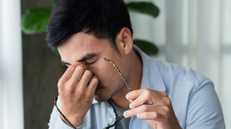 Man sitting at laptop puts his fingers to the bridge of his nose with glasses in hand