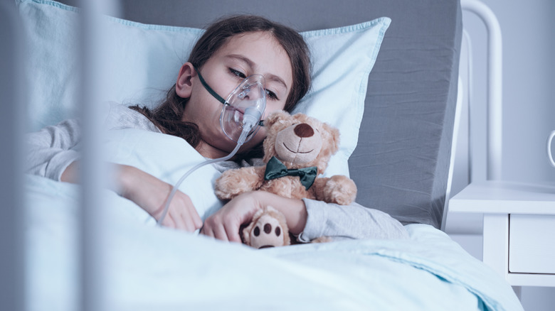 child wearing oxygen mask holding bear