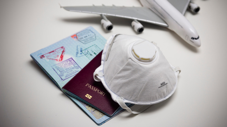 Mask, passport, and model airplane seated on white background