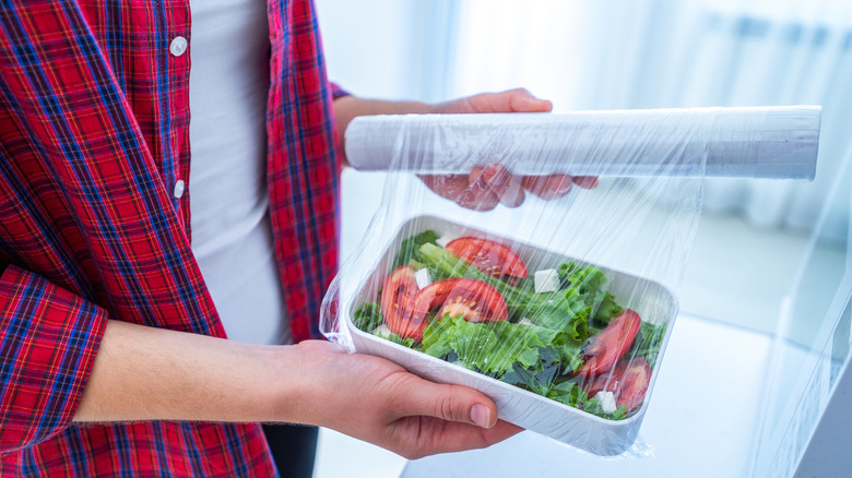 Person wrapping salad in Saran wrap