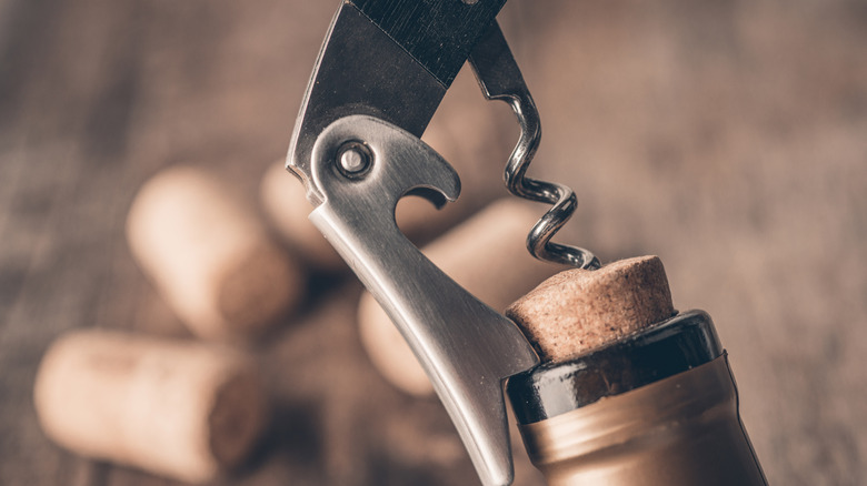 Corkscrew opening bottle of wine with corks in the background