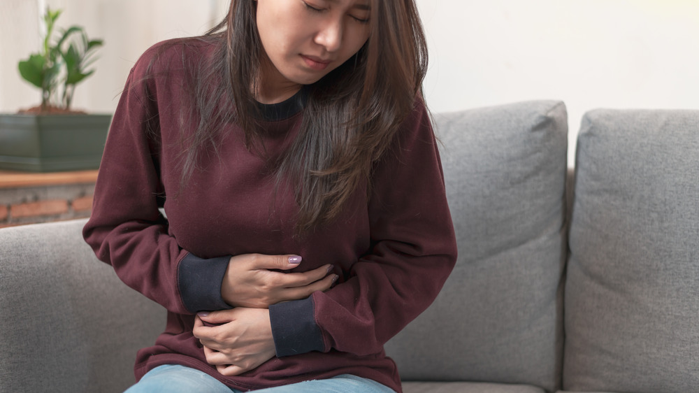 Woman sitting on couch clutching stomach in pain