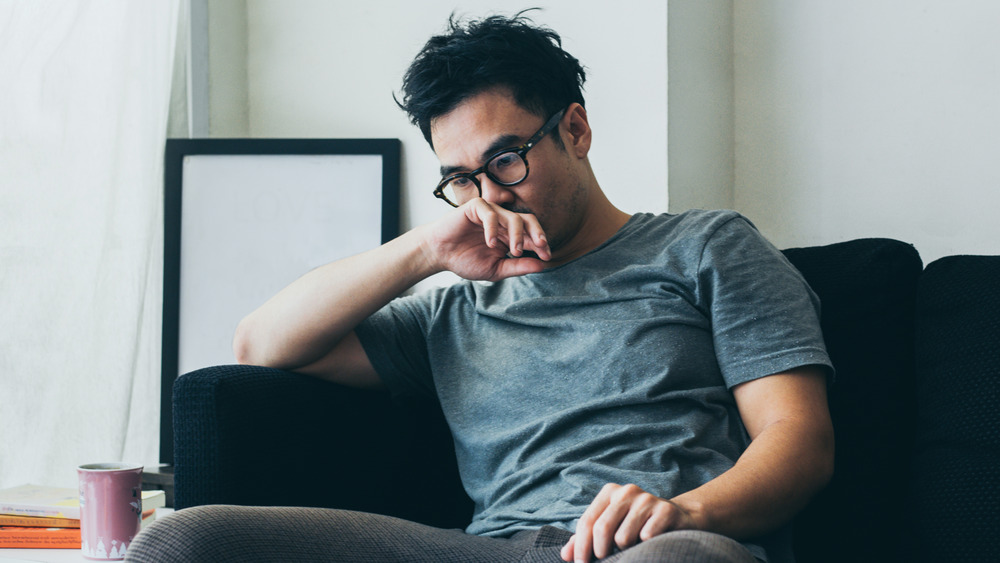 An emotional man with glasses sitting on his couch 
