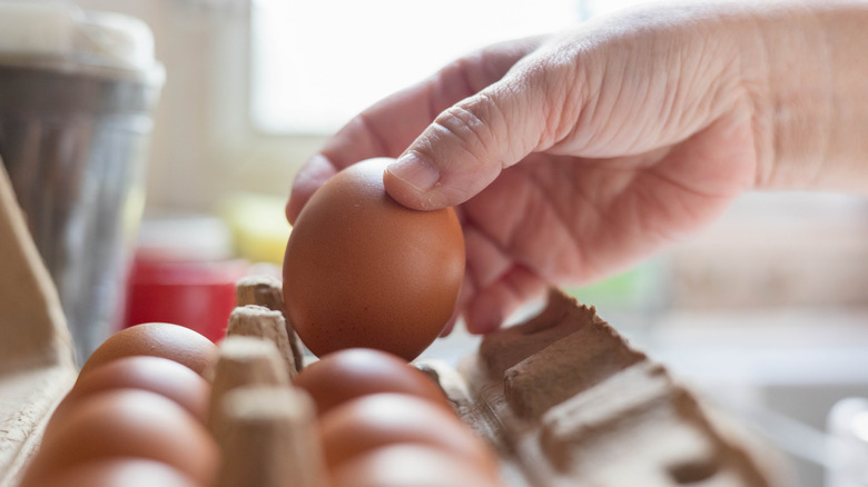 man's hand pulling brown eggs from carton